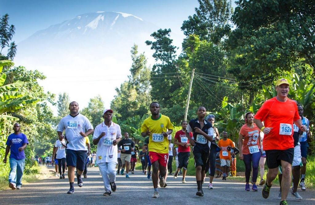 Many runners running on road with Mount Kilimanjaro in the background.